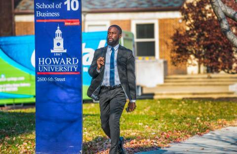 Photo of a bearded man in suit walking across HU campus